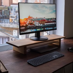 Peut inclure: Un moniteur d'ordinateur noir avec une image de ville sur l'écran est posé sur un support de moniteur en bois. Un clavier noir est sur un bureau en bois brun.