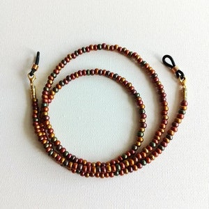 May include: A double-strand beaded eyeglass chain with gold-toned metal clasps. The beads are a mix of brown, copper, and green.