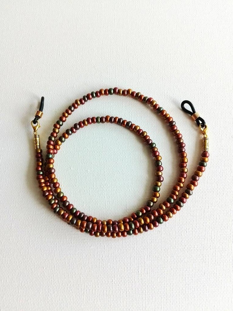 May include: A double-strand beaded eyeglass chain with gold-toned metal clasps. The beads are a mix of brown, copper, and green.