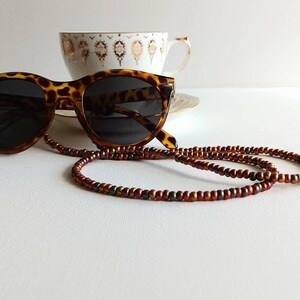 May include: Tortoise shell sunglasses with brown, red, and green beaded eyeglass chain.
