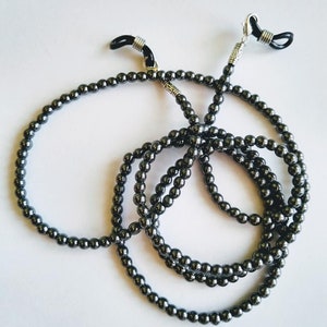 May include: A black beaded eyeglass chain with silver metal clasps. The chain is made of small, round beads and is designed to hold eyeglasses around the neck.