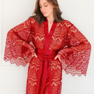 May include: A red lace robe with a satin sash. The robe has long sleeves and a V-neckline. The sash is tied at the waist.