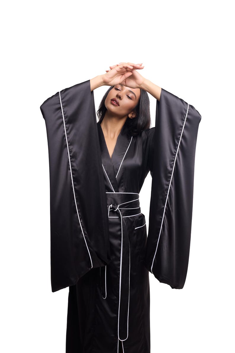 May include: A black satin robe with white piping. The robe has long sleeves and a sash tie at the waist.