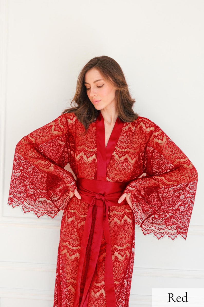 May include: A red lace robe with a satin sash. The robe has long sleeves and a V-neckline. The sash is tied at the waist.