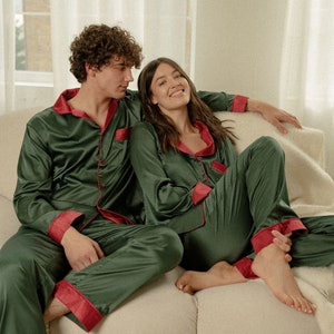 K&ouml;nnte beinhalten: Ein Paar tr&auml;gt passende gr&uuml;ne und rote Satin-Pyjamas und sitzt auf einem wei&szlig;en Sofa.