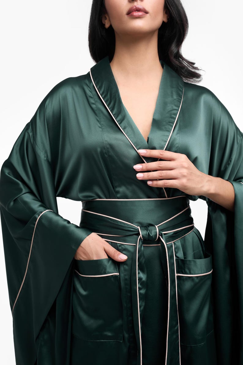 May include: A dark green satin robe with a white trim and a matching sash. The robe has long sleeves and two pockets.