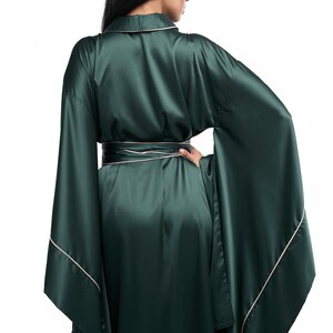 May include: A long, dark green satin robe with a white trim. The robe has a wide, flowing silhouette and long sleeves.