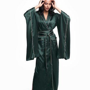 May include: A long, dark green satin robe with a white trim. The robe has a shawl collar, a tie belt, and two pockets. The robe is worn by a person with long dark hair.