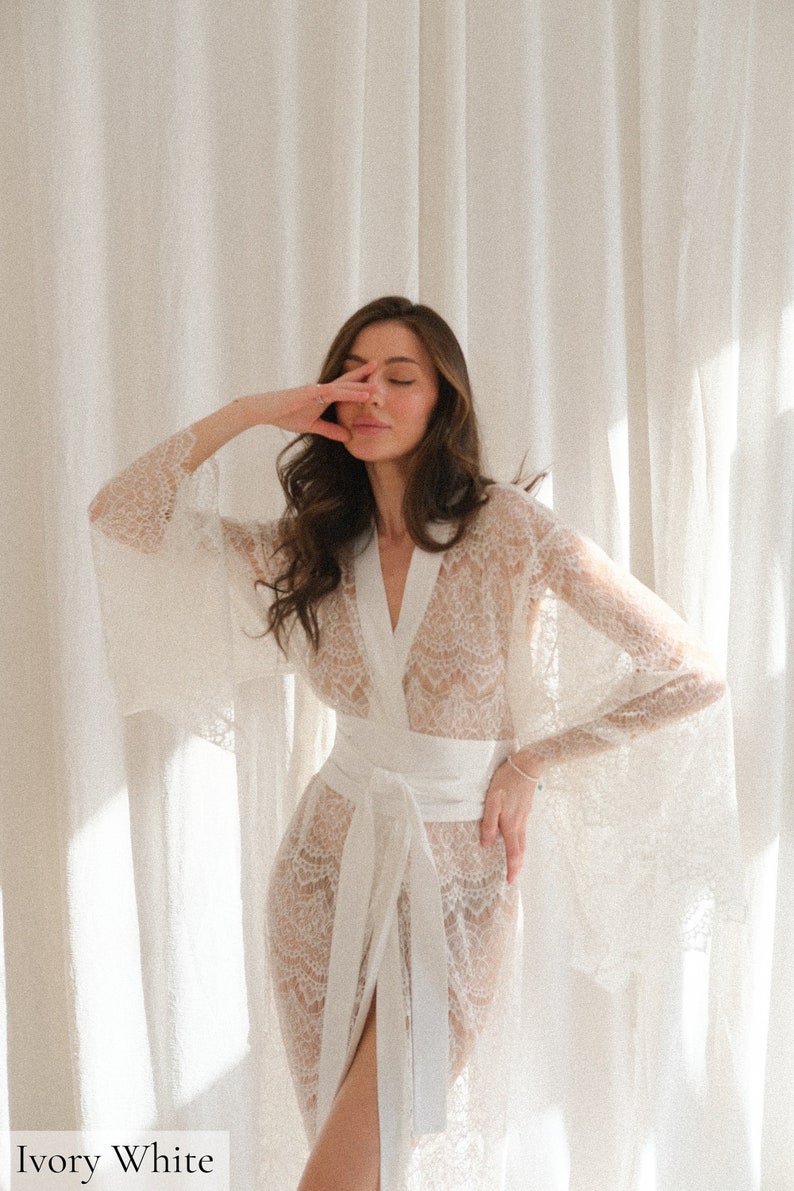 May include: A white lace robe with long sleeves and a sash tie. The robe is sheer and has a delicate floral pattern.