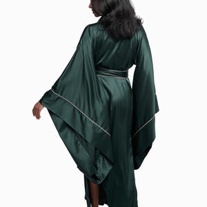 May include: A long, dark green satin robe with a white trim. The robe has wide sleeves and a sash that ties at the waist.