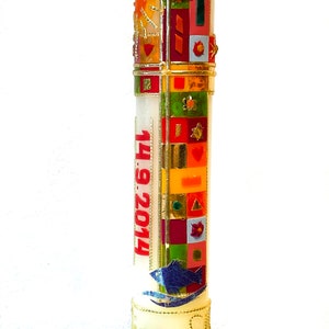 May include: A white candle with a gold and colorful design, the date "14.09.2014" and the word "Mira" on the base.