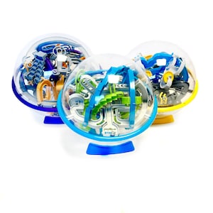 Op de afbeelding: Drie transparante plastic bolpuzzels met kleurrijke tracks en een blauw, geel en groen kleurenschema. De puzzels heten "Perplexus STAC"