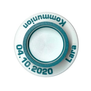 May include: White round ceramic disc with a teal blue ring around the edge. The disc has the text "Kommunion Lara 04.10.2020" printed in teal blue.