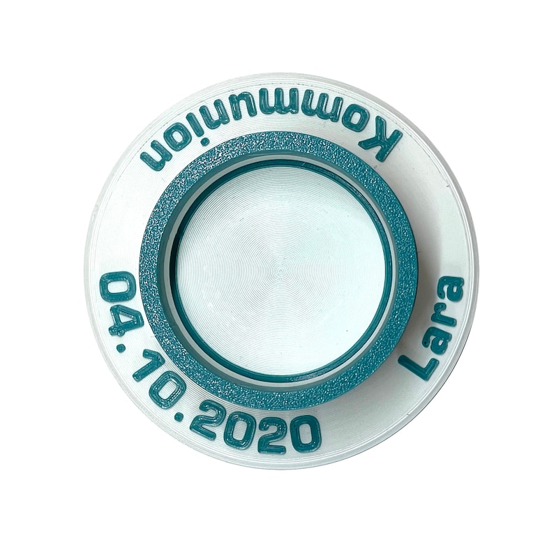 May include: White round ceramic disc with a teal blue ring around the edge. The disc has the text "Kommunion Lara 04.10.2020" printed in teal blue.