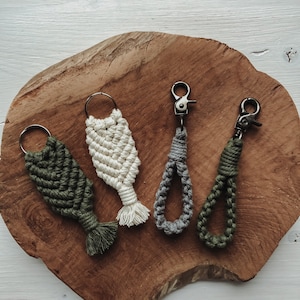 Pode incluir: Quatro chaveiros de macramé feitos à mão em diferentes cores e estilos. Os chaveiros são feitos com fibras naturais e apresentam uma variedade de nós e padrões. Os chaveiros são exibidos em uma superfície de madeira.