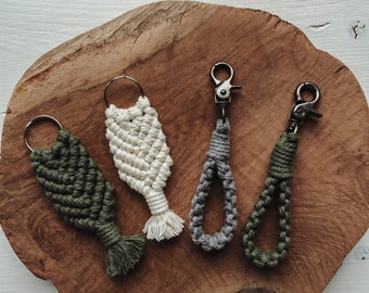 May include: Four handmade macrame keychains in different colors and styles. The keychains are made with natural fibers and feature a variety of knots and patterns. The keychains are displayed on a wooden surface.