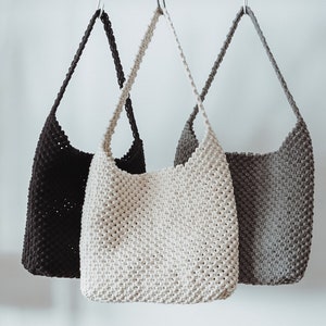 Peut inclure: Trois sacs cabas en crochet suspendus à des crochets. Les sacs sont faits d'une corde épaisse et sont en noir, blanc et gris.
