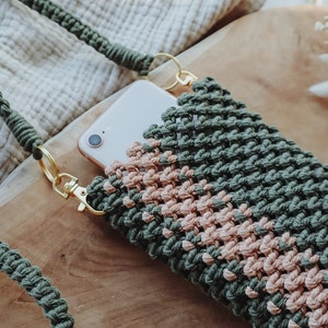 Könnte beinhalten: Eine gehäkelte Handyhülle in Grün und Rosa mit einem goldenen Kettenriemen. Die Hülle ist aus dickem, strukturiertem Garn gefertigt und hat ein schlichtes, modernes Design.