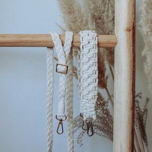 Puede incluir: Correas de bolso de macramé color crema con herrajes dorados y plateados. Las correas se muestran en una escalera de madera sobre un fondo neutro. Una correa presenta un diseño trenzado, la otra un patrón tejido.