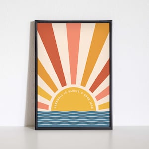 May include: A framed print featuring a retro sunburst design in shades of orange, yellow, and pink. The sun is yellow and has the text "Cornwall is always a good idea" around it. The bottom of the print shows a blue ocean with white waves.