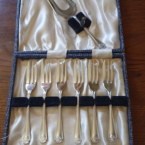 Könnte beinhalten: Ein Vintage-Silberbesteck-Set in einer blauen Box mit Satinfutter. Das Set enthält sechs Gabeln und zwei Servierutensilien. Die Gabeln sind ordentlich in der Box angeordnet, und die Servierutensilien sind darüber platziert. Das Set stammt wahrscheinlich aus der Mitte des 20. Jahrhunderts.