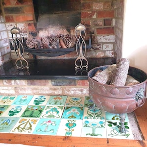 May include: A collection of square ceramic tiles featuring various floral and botanical illustrations in shades of blue, green, and yellow, arranged in a grid pattern, accompanied by a large, round, weathered copper basin with lion head handles.