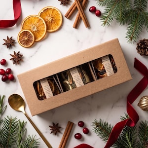 May include: A rectangular brown cardboard gift box with a clear window containing three separate pouches of dried potpourri ingredients. Each pouch features a label with instructions to add to a pot with water and simmer on low heat.
