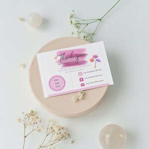 Può includere: Biglietto di ringraziamento rosa con un design floreale ad acquerello. Il biglietto include il testo "Grazie per il tuo acquisto" e spazio per un logo, link ai social media e un indirizzo email.