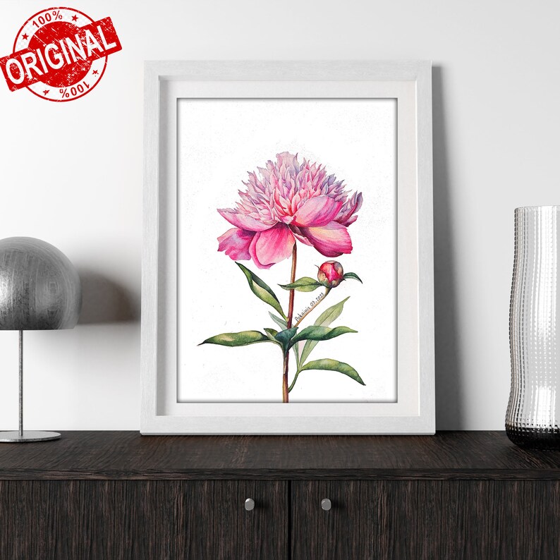 K&ouml;nnte beinhalten: Ein Aquarellbild einer rosa Pfingstrose mit gr&uuml;nen Bl&auml;ttern und einer Knospe. Das Bild ist in einem wei&szlig;en Rahmen gerahmt und befindet sich auf einer dunkelbraunen Oberfl&auml;che.
