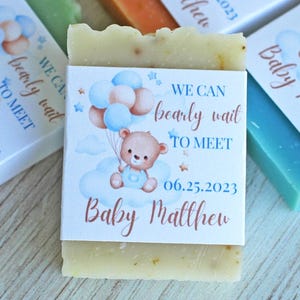 May include: A set of four favor soaps with blue and white labels. The labels feature a cartoon bear holding balloons and the text "We can barely wait to meet Baby Matthew" with the date "06.25.2023".