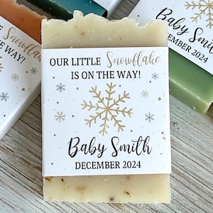 May include: White favor boxes with a snowflake design and the text "Our Little Snowflake is on the way!" and "Baby Smith" with a month and year.