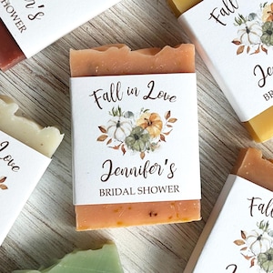 May include: Rectangular bars of soap wrapped in white paper bands. Each band features a watercolor illustration of pumpkins and autumn leaves with the text Fall in Love, Jennifer's BRIDAL SHOWER printed in black ink on the front of the packaging.