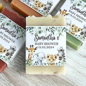 May include: Several bars of soap with decorative labels for a baby shower. The labels feature illustrations of safari animals like giraffes, elephants, and lions, along with the text "Samantha's BABY SHOWER 5.01.2024". The soaps are various colors.