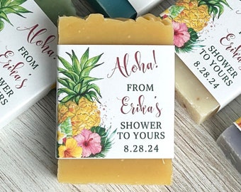 May include: A rectangular bar of soap wrapped in a white paper band featuring a watercolor illustration of a pineapple and tropical flowers. The text reads Aloha! FROM Erika's SHOWER TO YOURS 8.28.24 in a mix of script and sans-serif fonts.