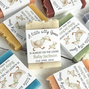 Puede incluir: Varias barras de jab&oacute;n de diferentes colores, cada una envuelta con una etiqueta que presenta una ilustraci&oacute;n de un ganso y el texto "A little silly Goose". Las etiquetas tambi&eacute;n incluyen el texto "Baby Jackson" y "Due April 2026".
