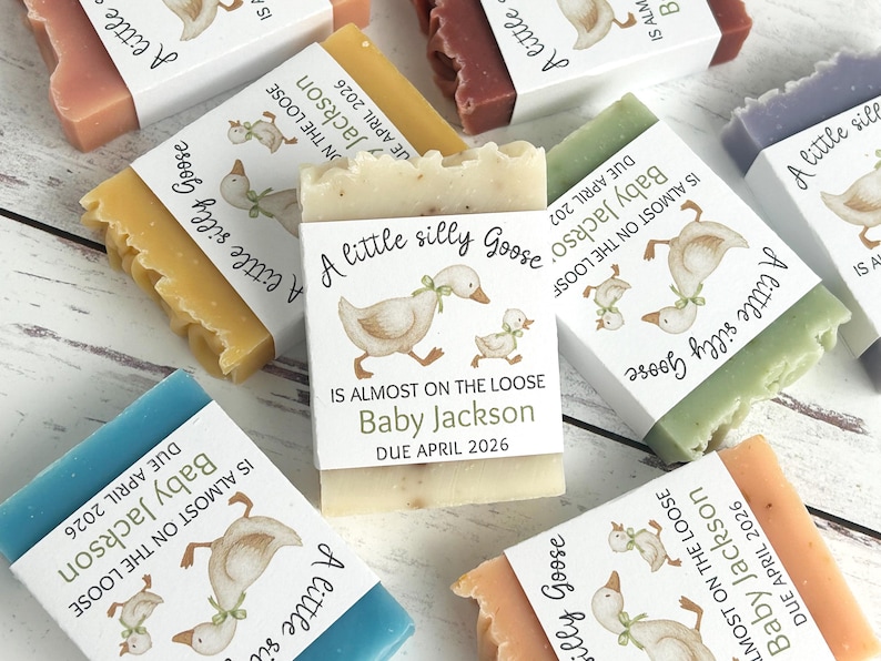 Puede incluir: Varias barras de jab&oacute;n de diferentes colores, cada una envuelta con una etiqueta que presenta una ilustraci&oacute;n de un ganso y el texto "A little silly Goose". Las etiquetas tambi&eacute;n incluyen el texto "Baby Jackson" y "Due April 2026".