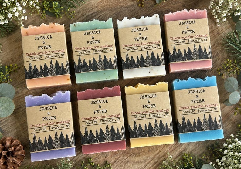 May include: Eight rectangular bars of soap in various colors including peach, green, white, pink, purple, maroon, yellow, and blue. Each bar is wrapped in a brown paper band printed with the text JESSICA & PETER, Thank you for coming!, 09.26.26, Catskill, NY.