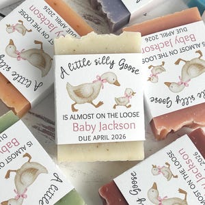 Puede incluir: Barras de jab&oacute;n de varios colores con etiquetas que presentan una ilustraci&oacute;n de acuarela de un ganso y un ganso. Las etiquetas dicen: "A little silly Goose, Is almost on the loose, Baby Jackson, Due April 2026."
