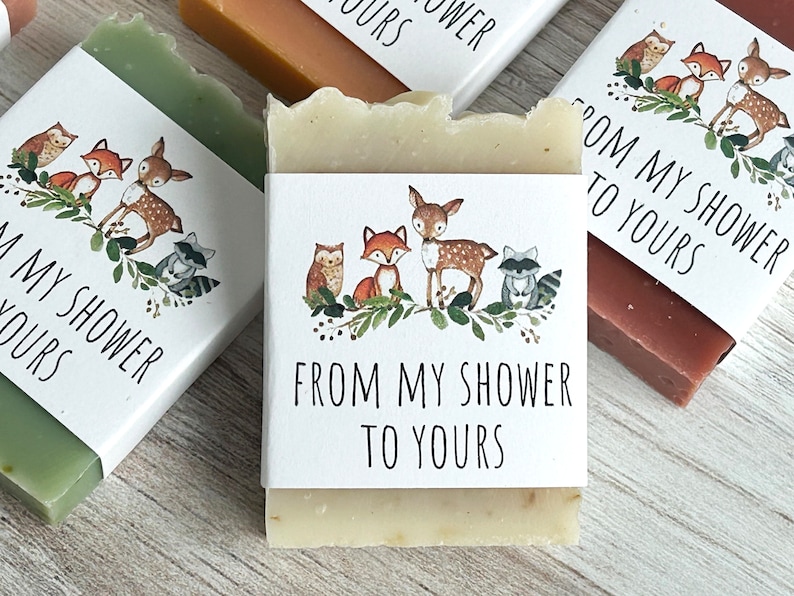 Pode incluir: V&aacute;rias barras de sab&atilde;o com r&oacute;tulos brancos com ilustra&ccedil;&otilde;es de animais da floresta e o texto "FROM MY SHOWER TO YOURS". Os sabonetes s&atilde;o de v&aacute;rias cores, incluindo verde, castanho e bege.