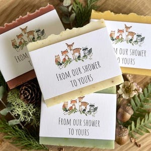 Puede incluir: Cuatro barras de jab&oacute;n hechas a mano con etiquetas que dicen "FROM OUR SHOWER TO YOURS". Cada etiqueta presenta una ilustraci&oacute;n de animales del bosque. Los jabones son de varios colores, incluyendo marr&oacute;n, amarillo y verde.