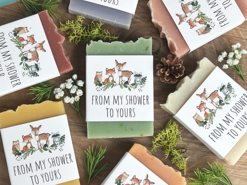 Puede incluir: Surtido de jabones artesanales de varios colores, cada uno envuelto con una banda de papel con ilustraciones de animales del bosque y el texto "FROM MY SHOWER TO YOURS". Los jabones est&aacute;n dispuestos con vegetaci&oacute;n decorativa.