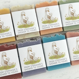 Puede incluir: Surtido de jabones hechos a mano en varios colores, cada uno envuelto con una etiqueta con una ilustraci&oacute;n de un ganso y un ganso. Las etiquetas dicen "FROM STEPHANIE'S SHOWER TO YOURS". Los jabones son de color amarillo, beige, naranja, verde, rojo, morado, azul y rosa.