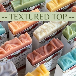 Puede incluir: Una variedad de jabones coloridos y texturizados en cajas decorativas. Los jabones son de varios colores, incluyendo rosa, azul, verde y amarillo. El texto "-- TEXTURED TOP --" se muestra en la imagen. Las cajas tienen patrones florales y texto.
