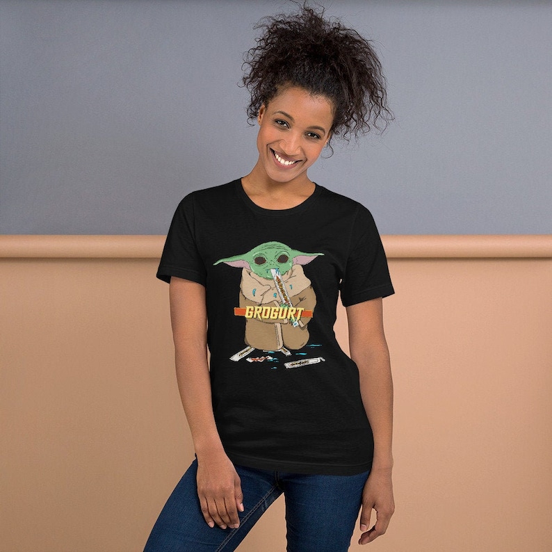Puede incluir: Una camiseta negra con un personaje de dibujos animados verde que sostiene un palo y el texto "GROGURT".