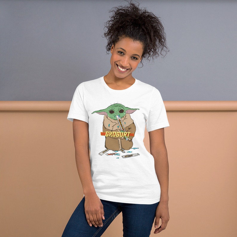 Puede incluir: Camiseta blanca con un personaje de dibujos animados verde que sostiene un palo marr&oacute;n y el texto "GROGURT".