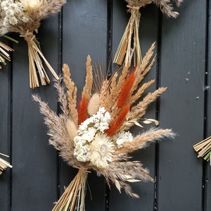 Pu&ograve; includere: Primo piano di bouquet di fiori secchi. I bouquet sono composti da grano, erba della pampa e altri fiori secchi in tonalit&agrave; beige, marrone e arancione. Legati con spago naturale, questi bouquet sono un elemento decorativo rustico.