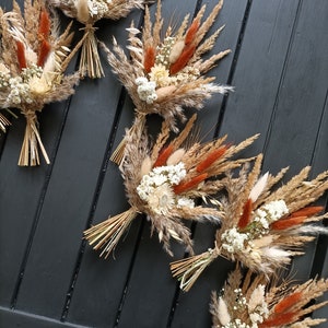 Pu&ograve; includere: Diversi bouquet di fiori secchi disposti su una superficie di legno scuro. I bouquet presentano un mix di erbe e fiori beige, marroni e color ruggine, legati con spago naturale. L'estetica generale &egrave; rustica e naturale.