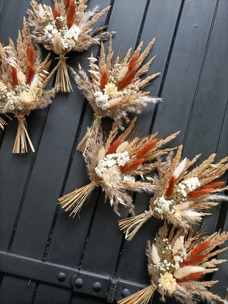 Pu&ograve; includere: Diversi bouquet di fiori secchi disposti su una superficie di legno scuro. I bouquet presentano un mix di erbe e fiori beige, marroni e color ruggine, legati con spago naturale. L'estetica generale &egrave; rustica e naturale.