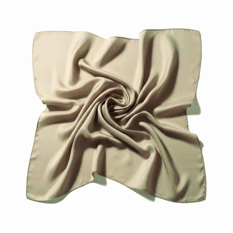 May include: A square, beige silk scarf with a swirling, folded design. The scarf has a smooth, lustrous texture and a subtle sheen. The edges are neatly finished, and the overall look is elegant and refined.