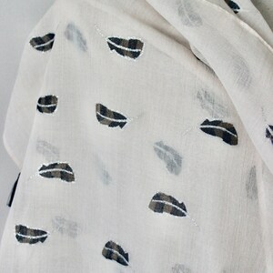 Peut inclure: Une &eacute;charpe blanche en voile avec un motif de plumes noires et brunes.